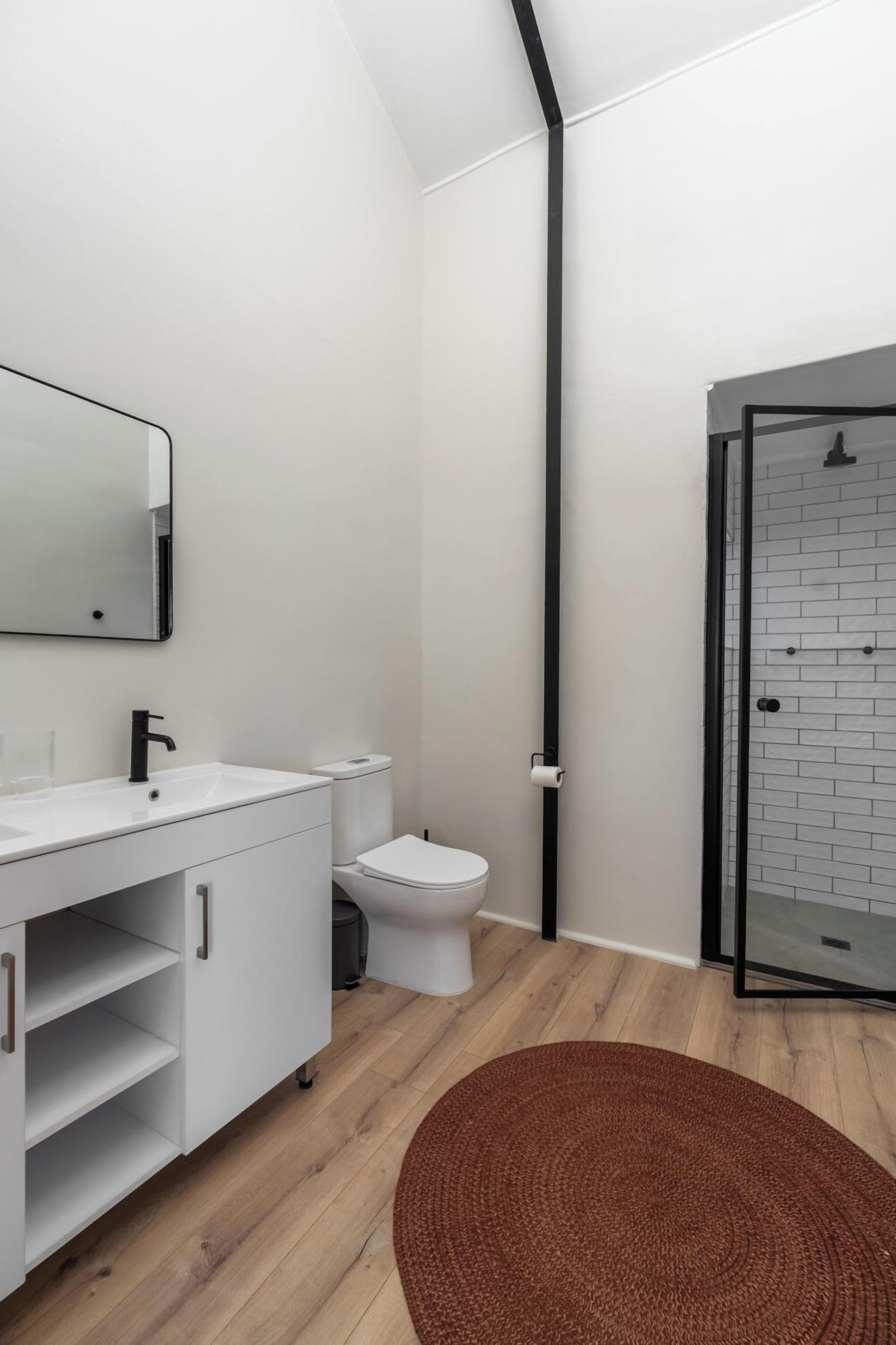 Un baño moderno con tocador blanco, grifo negro, inodoro blanco y cabina de ducha con mampara de vidrio.