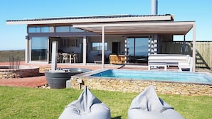 Ett modernt hus med pool, utomhusmöbler och en klarblå himmel.