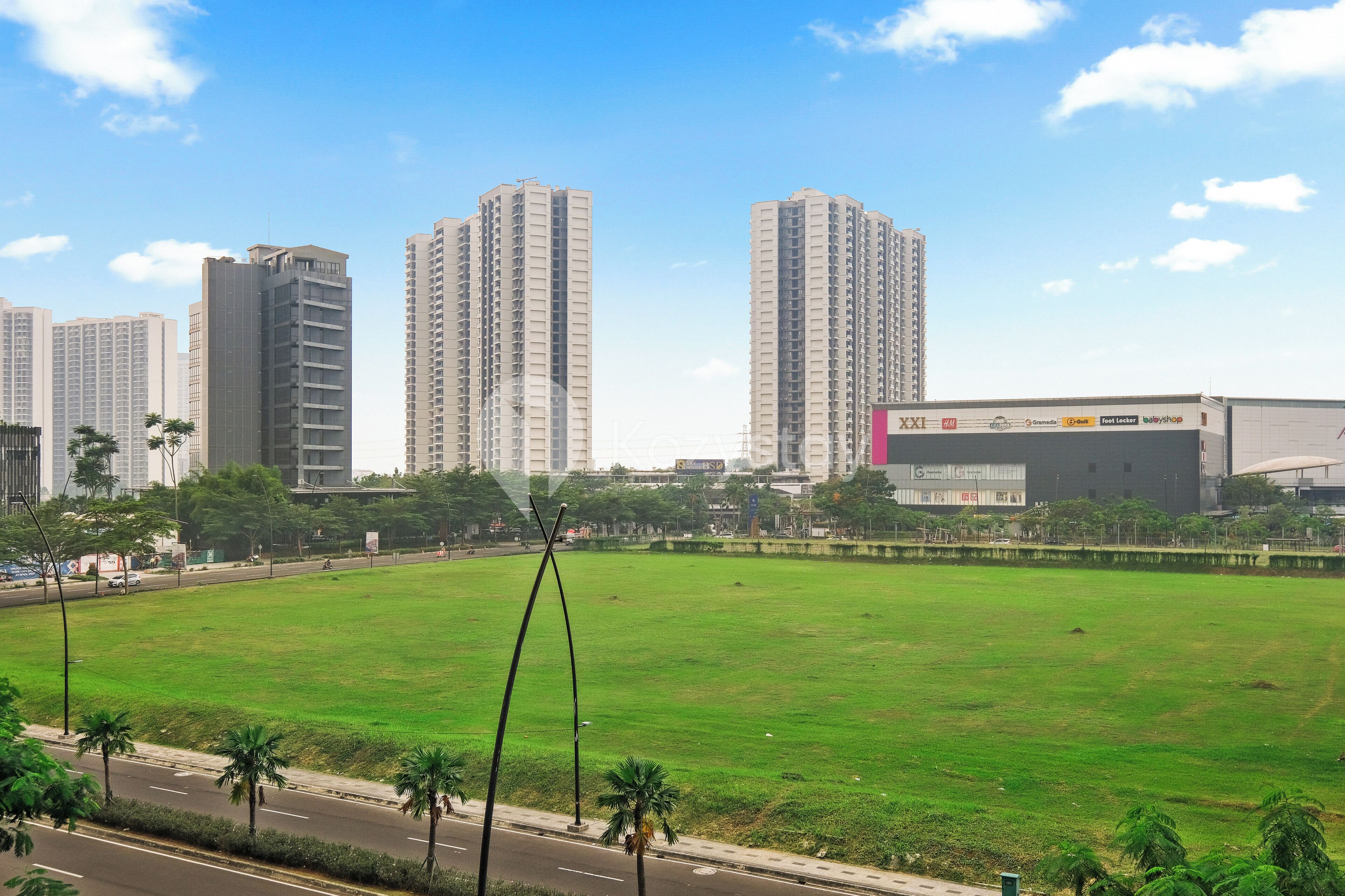 A grassy field with a road and tall buildings in the background.