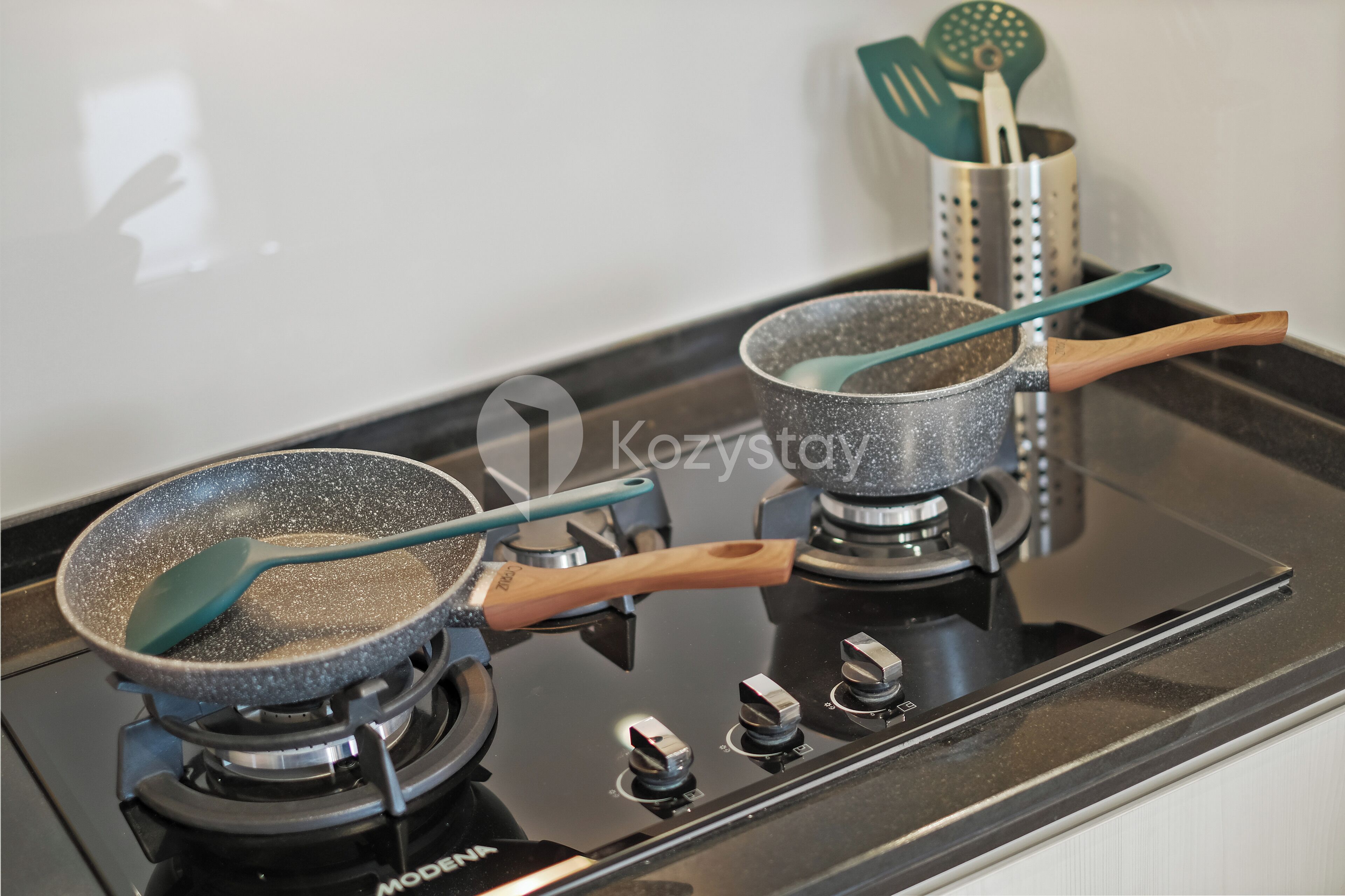 A kitchen with a stove, two frying pans, and a spatula holder.