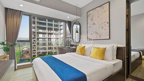 Una habitación de hotel moderna con una cama grande, un escritorio, una silla y un balcón con vistas a la ciudad.