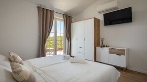 Un dormitorio con cama, armario, televisor y ventana con cortinas.