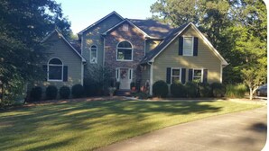 A two-story house with a front porch, a brick facade, and a well-maintained lawn. - Wooded Oasis: Safe & Secluded 2BR BASEMENT APT, Full Bath Retreat (Stockbridge)