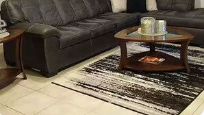 A living room with a dark leather sofa, a wooden coffee table, and a patterned rug. - Wooded Oasis: Safe & Secluded 2BR BASEMENT APT, Full Bath Retreat (Stockbridge)