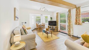 A living room with a sofa, a coffee table, a TV, and a dining area with chairs and a table. - Host & Stay | LOOK Flat (Scarborough)