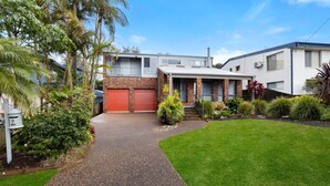 A two-story house with a brick facade, a red garage door, and a well-maintained lawn. - Lumina - Fireplace - 3 Mins Walk to Beach (Culburra Beach)