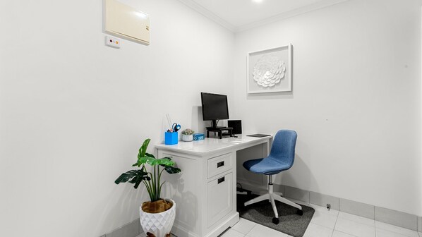 Un espacio de oficina moderno con un escritorio blanco, una silla de oficina azul, un monitor de computadora y una planta en maceta.
