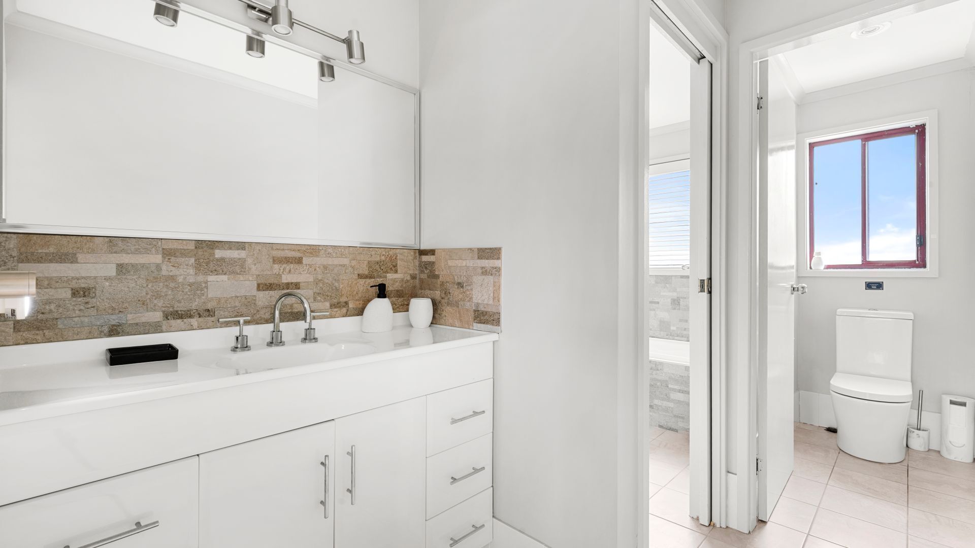 A modern bathroom with a white sink, a beige and brown tiled backsplash, and a white toilet.