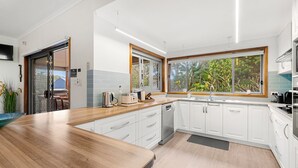 A modern kitchen with white cabinets, a wooden countertop, and a large window offering a view of greenery. - Lumina - Fireplace - 3 Mins Walk to Beach (Culburra Beach)