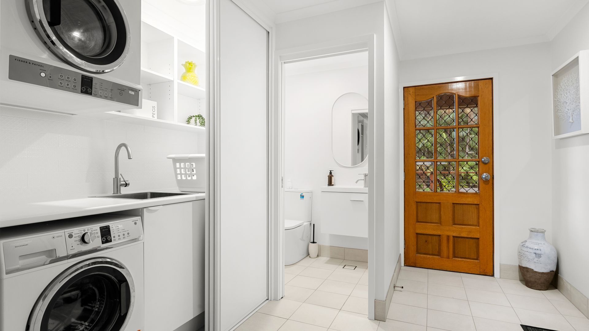 Un espace buanderie comprenant un lave-linge, un évier et un miroir.
