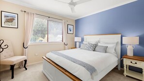 Un dormitorio con cama, mesitas de noche, una silla y una ventana con persianas.