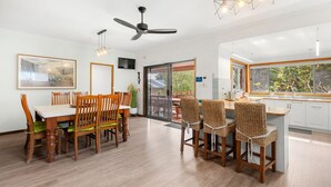 A modern kitchen with a dining area, wooden furniture, and a view of greenery outside. - Lumina - Fireplace - 3 Mins Walk to Beach (Culburra Beach)