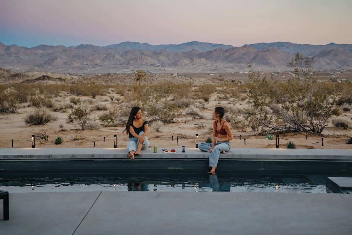 Two people sitting by a pool with a desert landscape in the background.