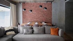 Un soggiorno moderno con una parete in mattoni, un tavolo da pranzo apparecchiato per sei persone e un divano grigio con cuscini decorati.