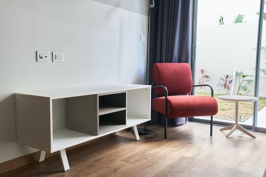 Une pièce moderne avec une console blanche, une chaise rouge et une petite table ronde.
