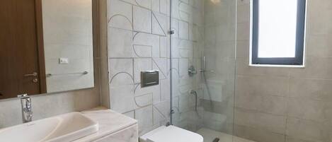 A modern bathroom with a glass shower enclosure, a marble sink, and a toilet.