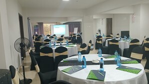 A conference room with multiple tables, each with water bottles, notebooks, and chairs with black and gold sashes. - Downtown ecopark hotel (Kitui)