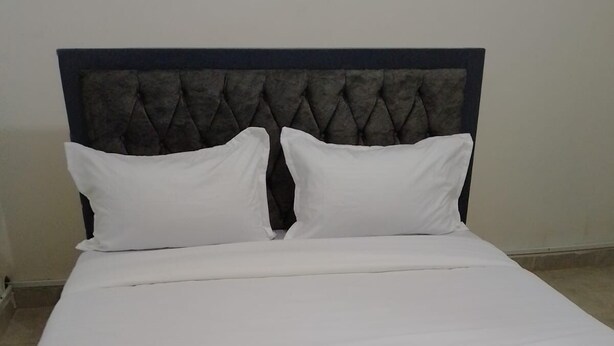 A neatly made bed with a dark headboard and white bedding. - Downtown ecopark hotel (Kitui)