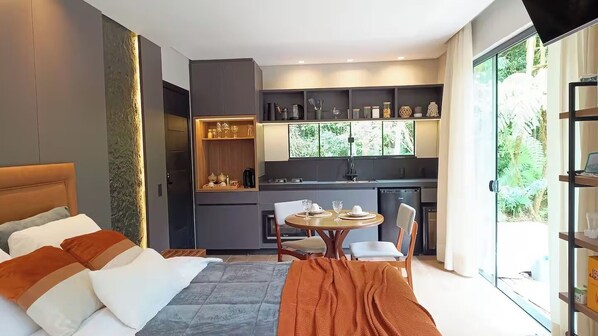 A modern hotel room with a bed, a small dining table, and a kitchenette. - Lion's Lodge in Rancho Queimado (Rancho Queimado)