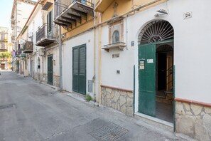 Eine enge Straße mit Gebäuden, die Steinwände, grüne Fensterläden und Balkone zeigen.
