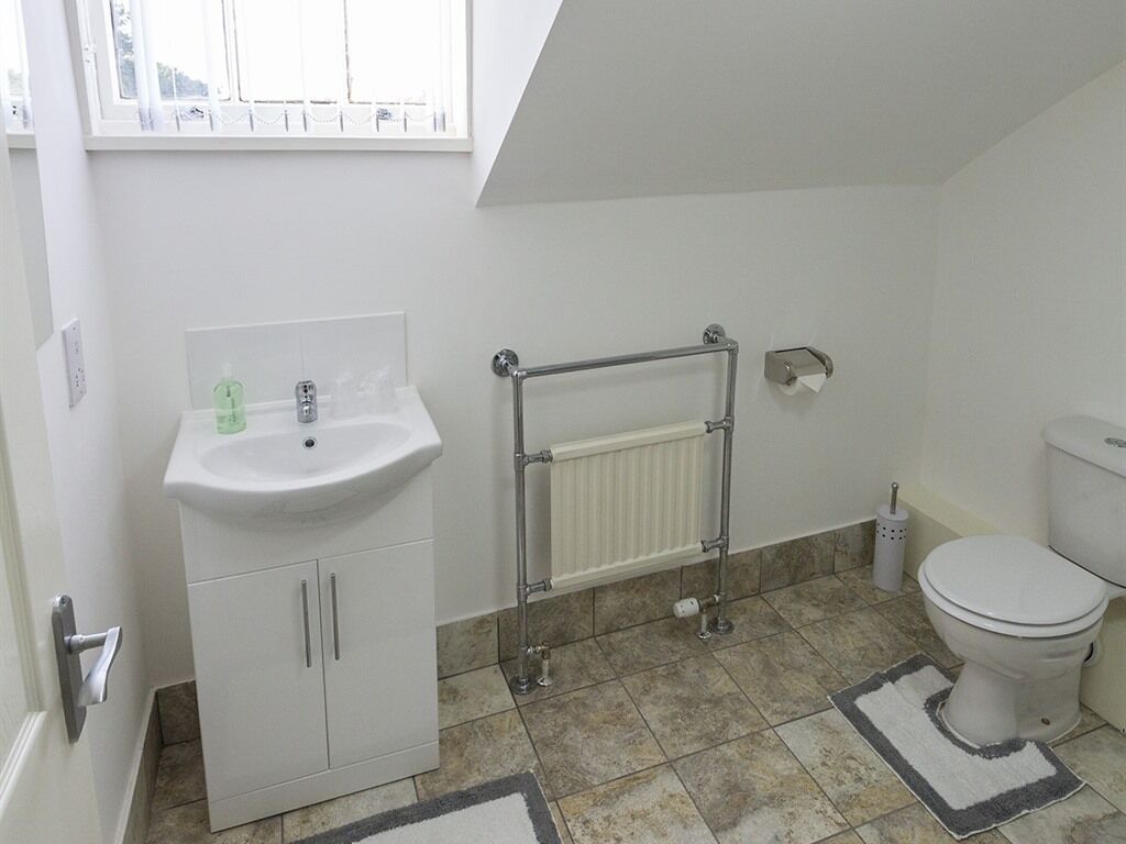 A bathroom with a white sink, a radiator, a toilet, and a window above the sink.