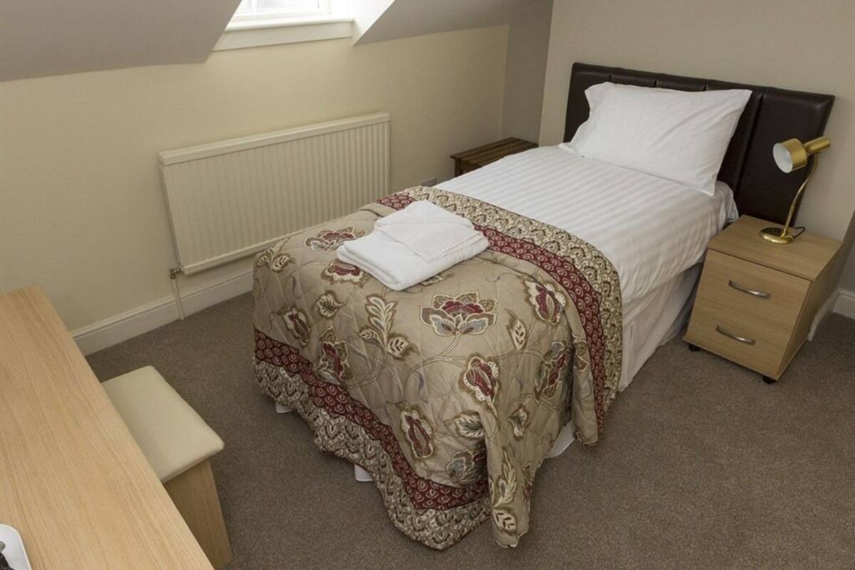 A bedroom with a bed, bedside table, lamp, and a window.