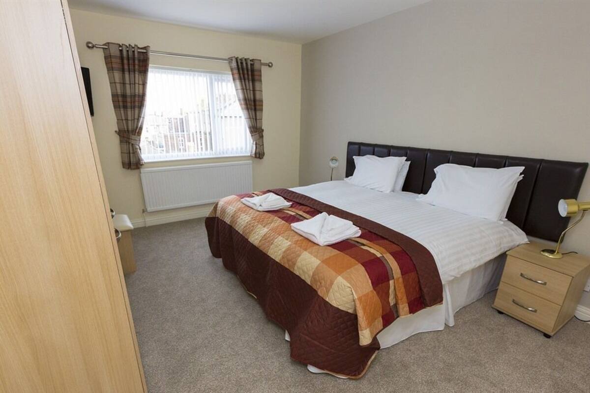 A bedroom with a bed, a bedside table, a lamp, and a window with curtains.