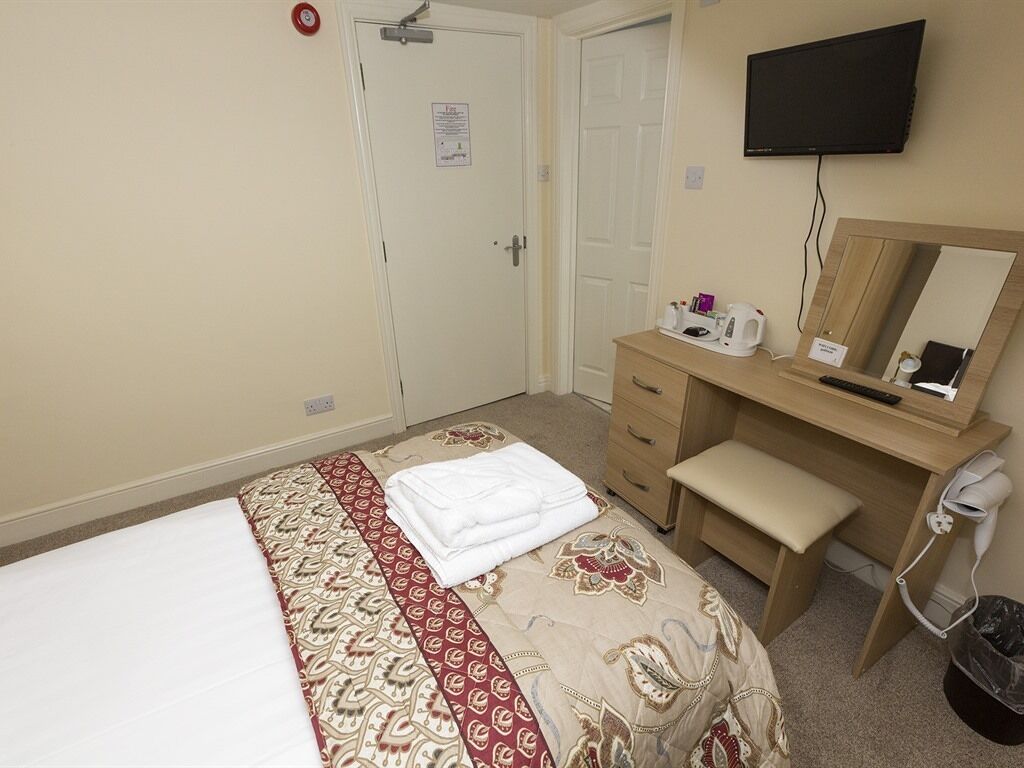 A hotel room with a bed, a desk with a mirror, a television, and a small trash bin.