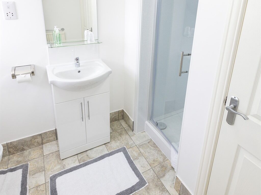 A bathroom with a white sink, mirror, and cabinets, a glass shower enclosure, and a white door.