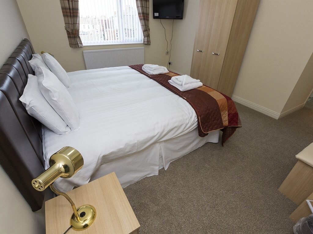 A hotel room with a bed, a bedside table with a lamp, a wardrobe, and a television on the wall.
