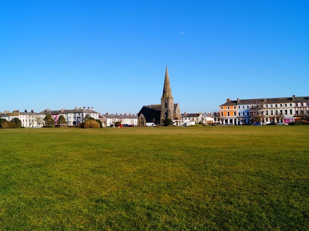 A grassy field with a church and residential buildings in the background.