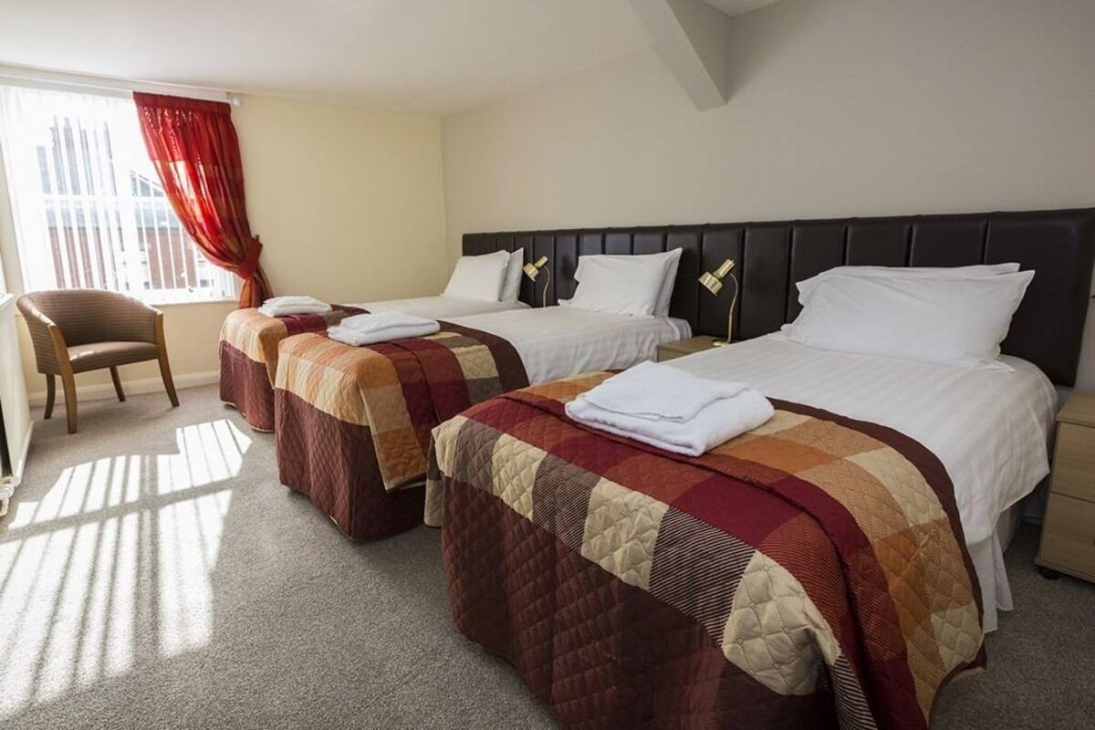 A hotel room with two beds, a chair, and a window with red curtains.