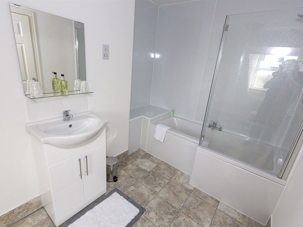 A modern bathroom with a white sink, mirror, and glass shower enclosure.