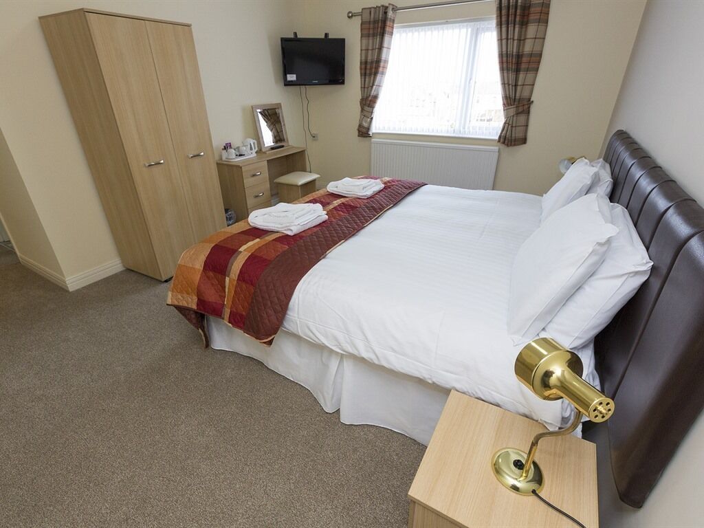A hotel room with a bed, a wardrobe, a bedside table with a lamp, a television, and a window with curtains.