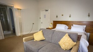 Una habitación de hotel con un sofá gris, una cama con cabecera de madera y una mesita de noche con lámpara.
