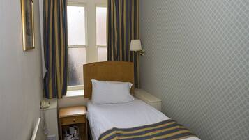 A hotel room with a single bed, a bedside table, a lamp, a telephone, and a window with curtains.