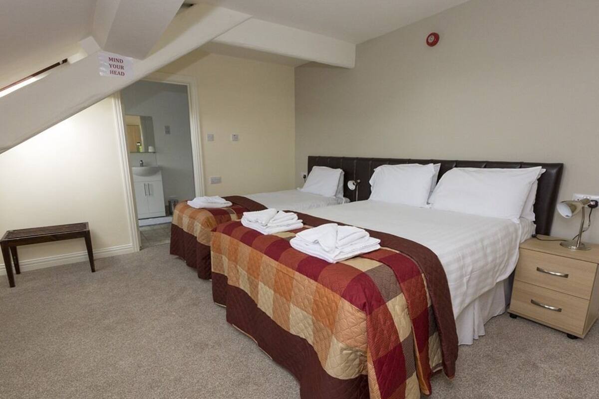 A hotel room with a large bed, two bedside tables, a bench, and a sign on the ceiling.