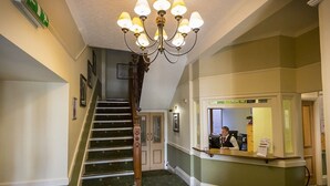 Un vestíbulo de hotel con una gran escalera, una recepción y una araña.