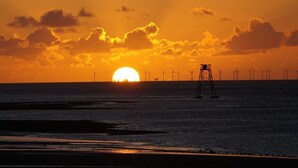 Atardecer sobre el océano con aerogeneradores a lo lejos.