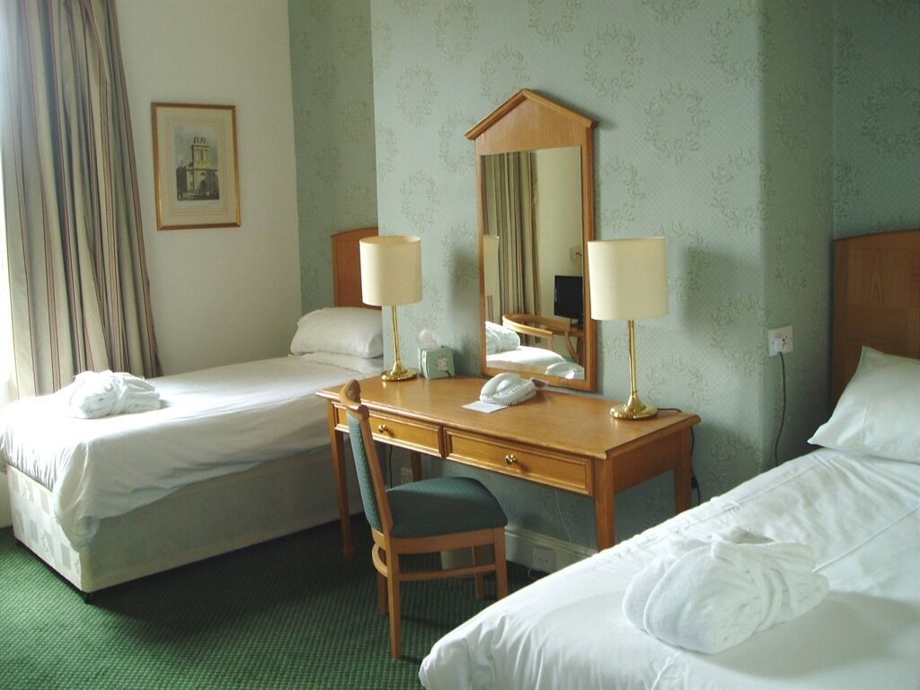 Habitación de hotel con dos camas individuales, un escritorio de madera con silla, teléfono y espejo.