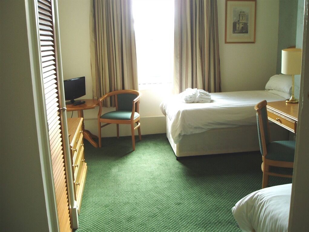 Habitación de hotel con cama, escritorio, silla, televisión y ventana con cortinas.