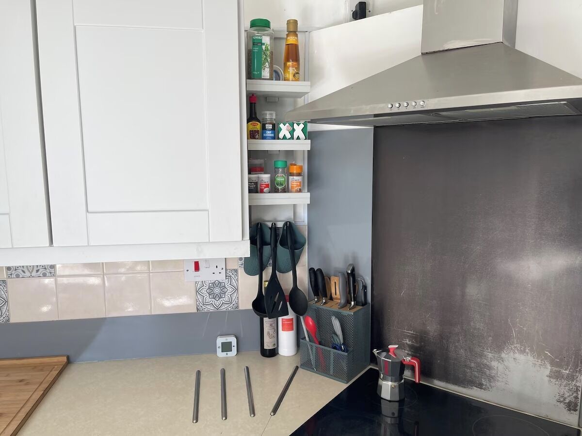 A kitchen with white cabinets, a stainless steel range hood, and various kitchen utensils and appliances.