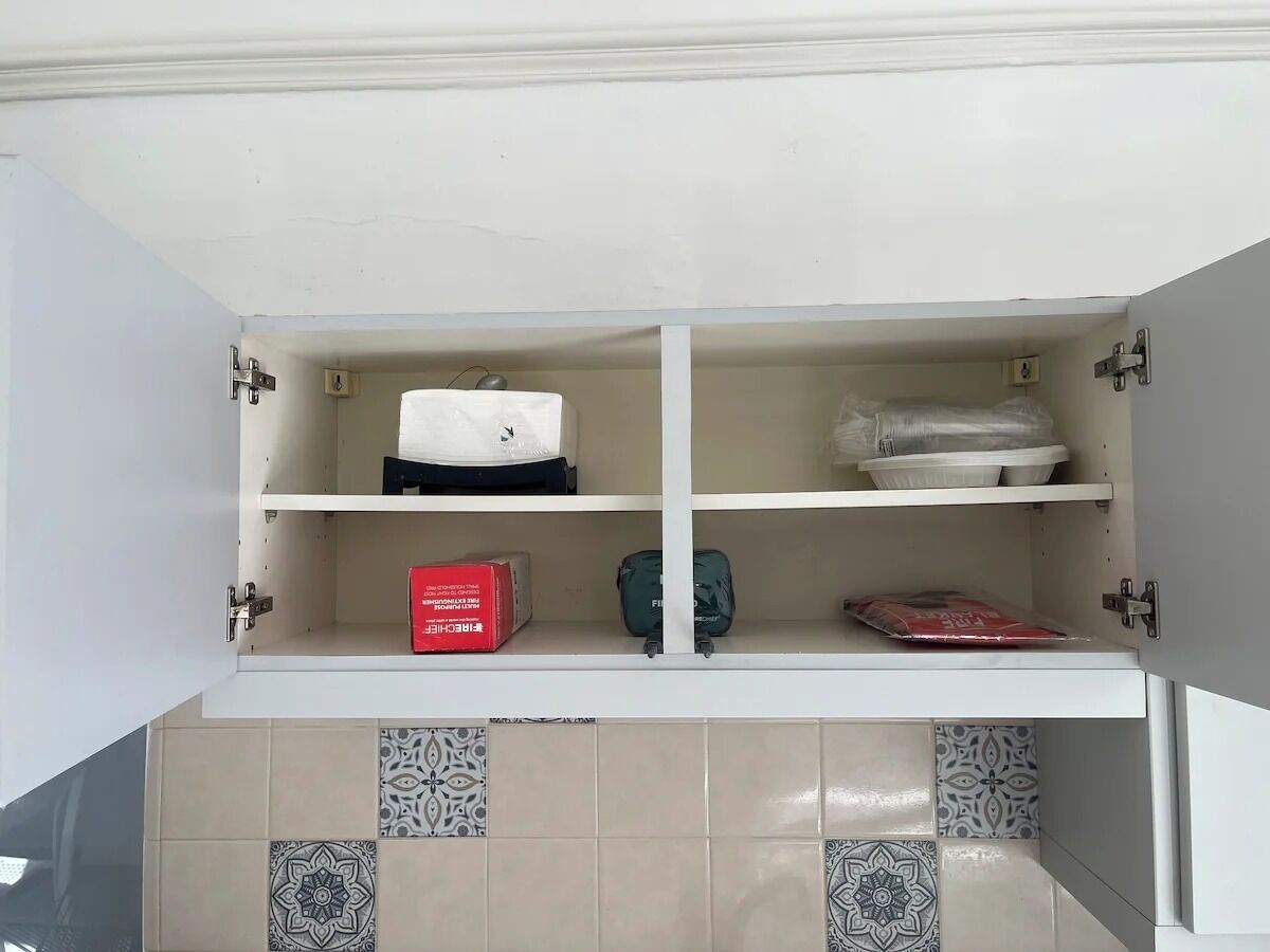 Ett köksskåp med två hyllor, varav den ena innehåller en vit apparat, en röd låda och en grön påse; den andra hyllan innehåller en vit behållare och ett rött paket.