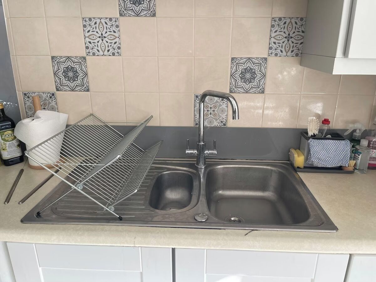 A kitchen with a double sink, a drying rack, and various kitchen items on the counter.