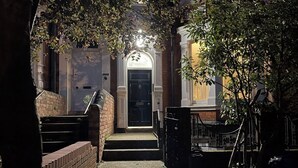 Un stretto vicolo che conduce a un edificio con una porta nera, gradini in mattoni e un piccolo albero.