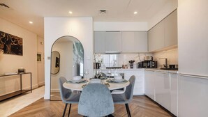 A modern kitchen with white cabinets, a dining area with a round table and grey chairs, and a large mirror on the wall. - Lux 2BR Downtown Enjoy Full Burj Khalifa View (Dubai)