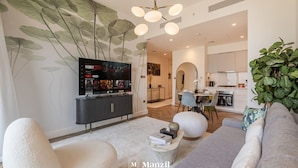 A modern living room with a flat-screen TV, a dining area, and a kitchen. - Lux 2BR Downtown Enjoy Full Burj Khalifa View (Dubai)