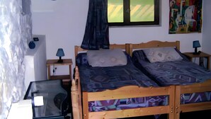 A bedroom with a wooden bed, two bedside tables with lamps, a window with curtains, a wall clock, and a colorful painting. - Farm Cottage "La Grange" (Garde-Colombe)