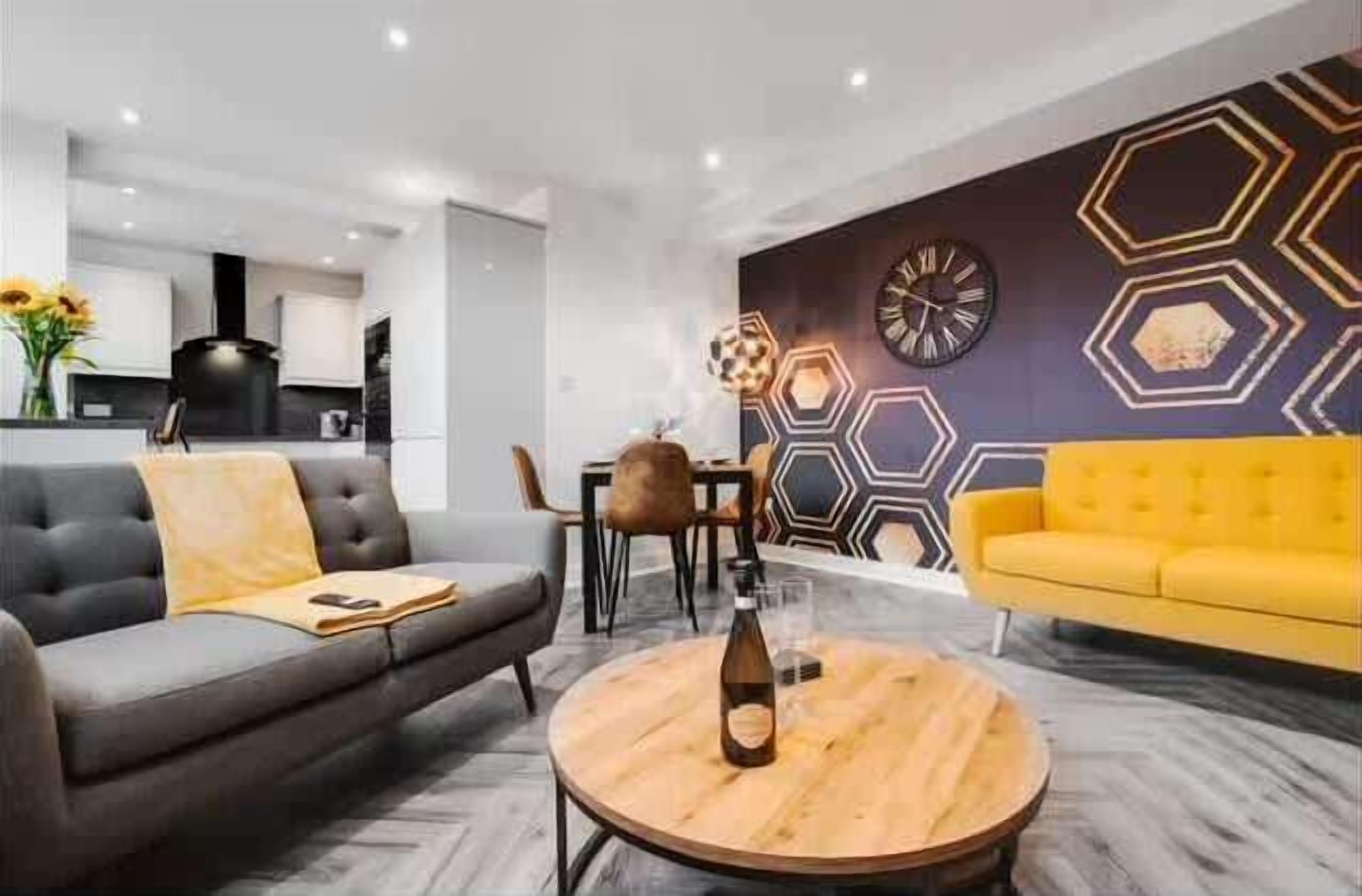 A modern living room with a sofa, a yellow armchair, a round coffee table, and a hexagonal-patterned wall.