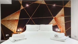 Une chambre d’hôtel moderne avec une tête de lit à motifs géométriques, un lit parfaitement fait avec du linge de lit blanc et deux lampes de chevet.